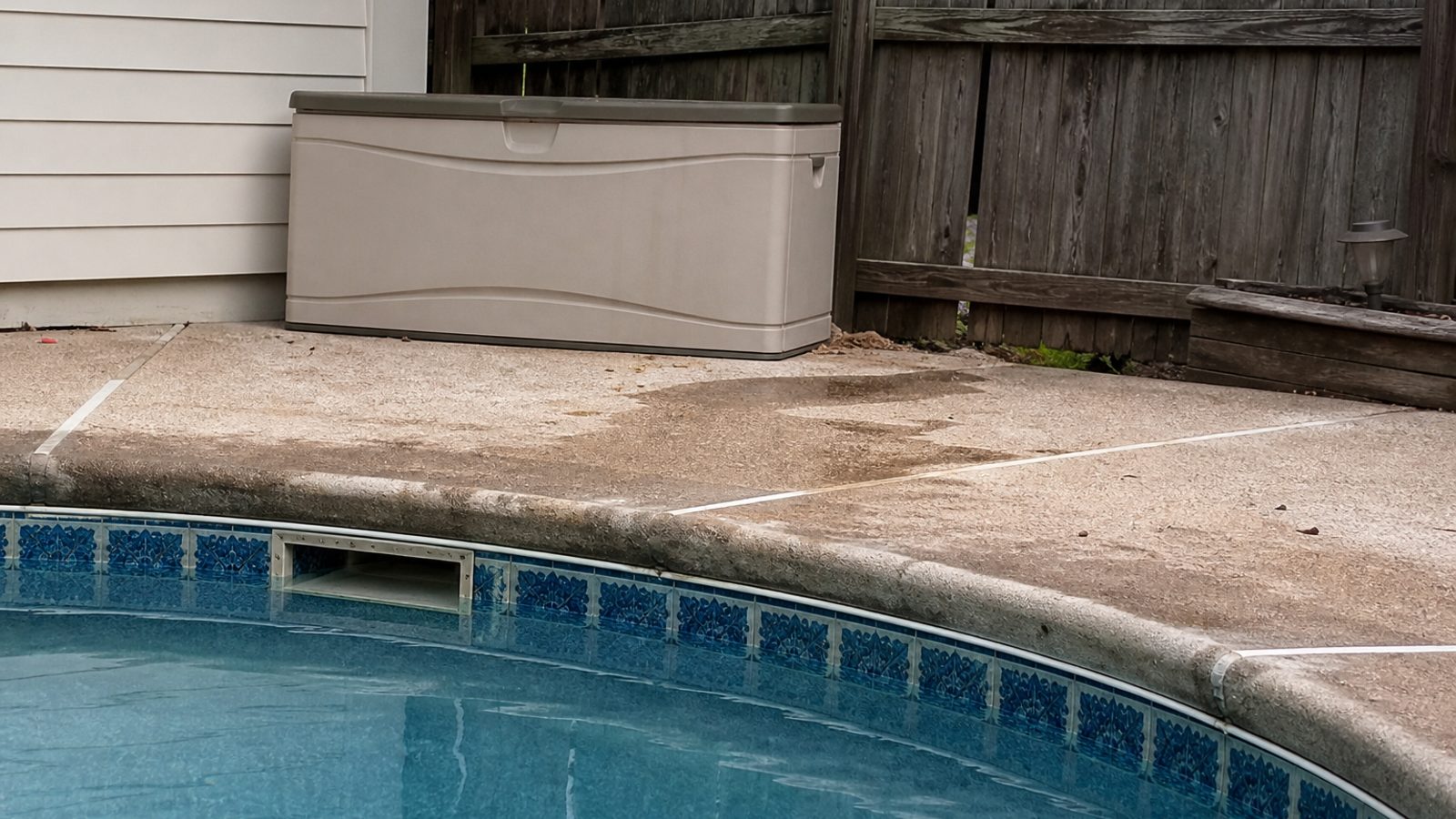 Pool deck edge near skimmer with subtle wet area and weathered coping, realistic residential pool