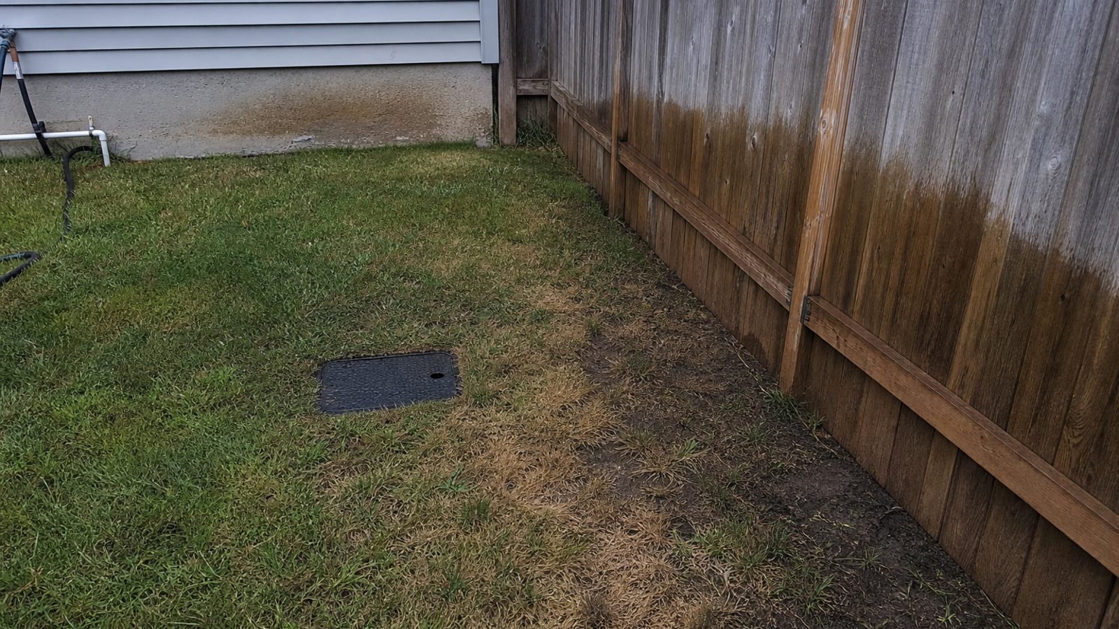 Residential side yard sprinkler zone with overspray stain on fence and dry patch near valve box